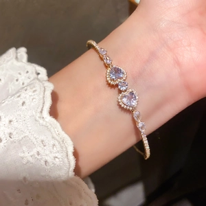 Close-up of golden open bracelet with lavender heart-shaped stones and zircons