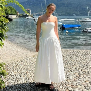Elegantes weißes trägerloses Maxikleid mit fließendem Saum am See in Urlaubsstimmung