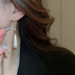 Détail de longues boucles d'oreilles dorées avec zircons et perles en goutte sur modèle