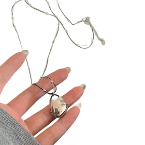 Handheld silver teardrop pendant necklace with delicate beaded chain on grey sweater