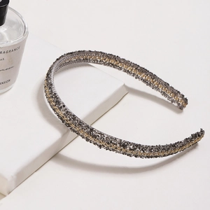 Sparkling dark grey headband with gold chain accent on a white geometric stand