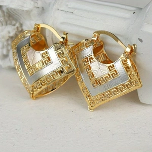 Macro detail of gold and silver shield earrings featuring an intricate Greek Key pattern