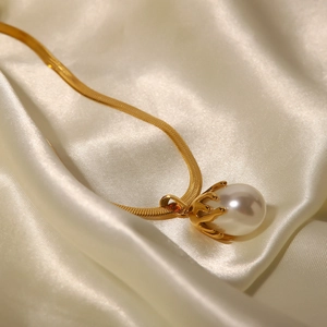 Close-up of a white round pearl pendant on a gold snake chain over silk fabric