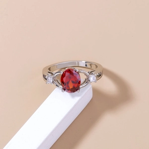 Elegant silver ring with oval red gemstone and clear zircon accents on a clean pedestal