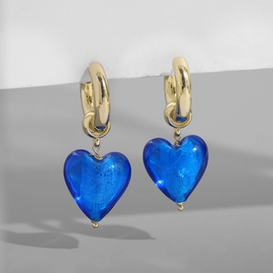Gros plan de créoles dorées avec pendentifs en forme de cœur en verre bleu et dorure