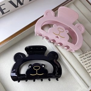 Close-up of pink and black bear hair claws with gold outlines on a beige velvet jewelry tray