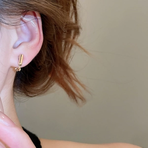 Close-up of golden geometric screw-on ear clip converter on ear with a small gold cylinder