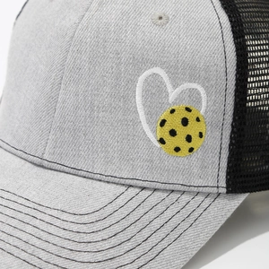 Detailed embroidery of a white heart and yellow pickleball on a mesh trucker hat