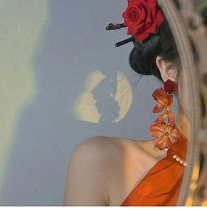 Artistic detail of red floral long earrings and rose hair pin on model with silhouette lighting