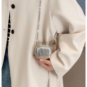 Mini silver metallic suitcase style crossbody bag with chain strap on a white coat