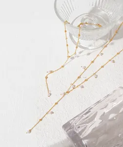 Detail of 18k gold plated titanium necklace with delicate pearls on a beige surface