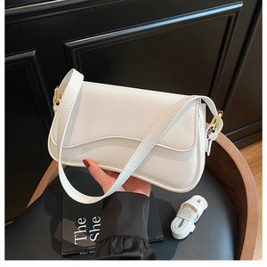 Detail of white leather shoulder bag with gold hardware and extra strap on a dark texture