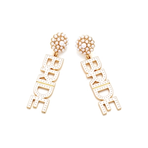 Macro detail of gold bridal earrings featuring BRIDE letters with faux pearl accents