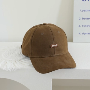 Detail of brown cotton baseball cap featuring white 'good' embroidery on smooth canvas