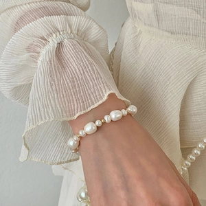 Close-up of fresh water pearl and gold bead bracelet on a model wearing cream fabric