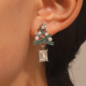 Close-up of Christmas tree earrings with green zircons and white pearls worn on ear