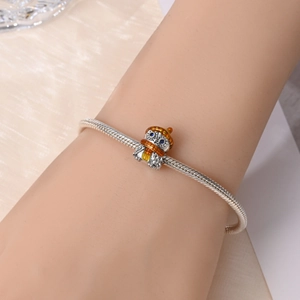 Detailed view of silver owl charm with orange enamel hat and blue gem eyes on a bracelet