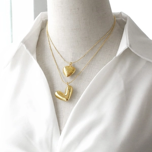 Double layered heart pendant necklace in polished gold finish on white shirt