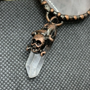 Detailed view of vintage bronze skull charm attached to a transparent crystal column pendant