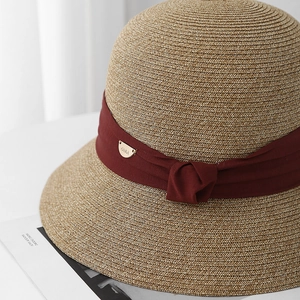 Détail du chapeau de paille avec ruban bordeaux et pendentif en métal doré