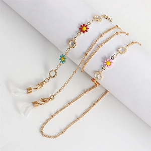 Detail of gold eyewear chain with colorful flower charms and acrylic rings on a white stand