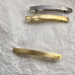 Detailed view of matte brushed metal hair clips in gold and silver finishes on white fabric