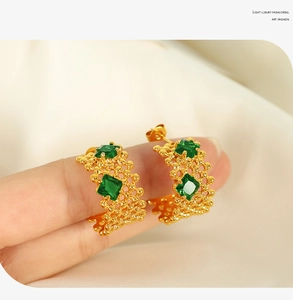 Détail macro de boucles d'oreilles dorées en C avec zircon vert sur fond de soie