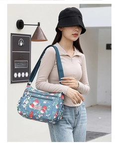 Detailed side view of floral crossbody bag with multiple zippers and wide strap on model