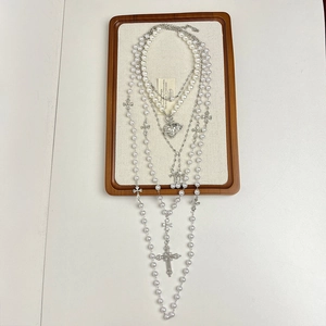 Close-up of layered pearl and silver cross necklaces on a wooden jewelry display stand