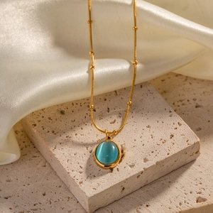 Macro shot of gold plated necklace with blue cat eye stone on white silk and stone