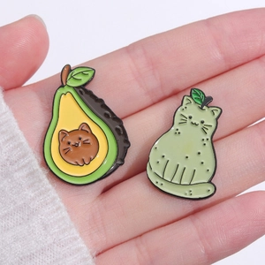 Detailed view of two cute cat avocado enamel pins displayed on a person's palm