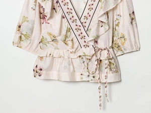 Detail of floral wrap top with V-neckline, ruffle hem, and light pink waist tie