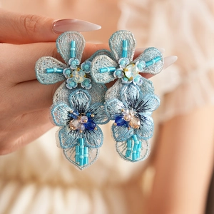 Macro detail of blue embroidered floral earrings with beads and crystal accents