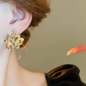 Close-up of golden hollow flower stud earring with textured metal petals on model