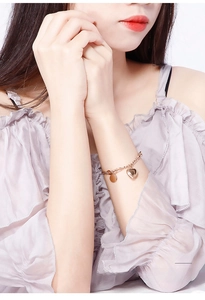 Macro detail of rose gold heart pendant bracelet on model wrist with polished round tag