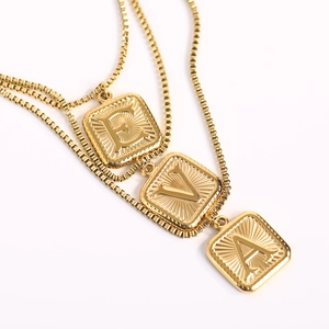 Detailed macro view of triple layer gold plated square pendants engraved with letters E, V, A