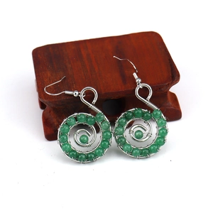 Detailed close-up of handmade green stone spiral earrings on a dark wood stand
