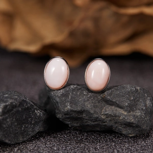 Macro view of two pink oval jasper gemstones in dark metal settings on black rock