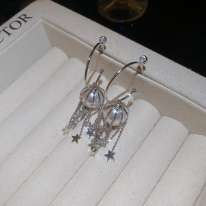 Detail of silver tassel earrings featuring pearls and sparkling star charms on a velvet box