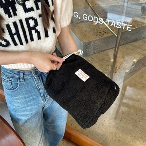 Detail of soft black faux shearling makeup bag with drawstring closure and quote patch