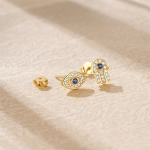 Detail of Hamsa Hand and Evil Eye gold earrings with blue and white zircon stones