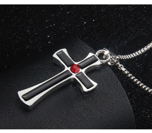 Detail of silver cross necklace with black inlay and red rhinestone on black leather