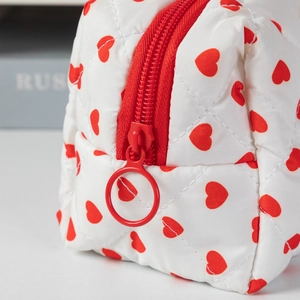 Macro shot of white quilted heart pattern makeup bag with a red zipper and round pull