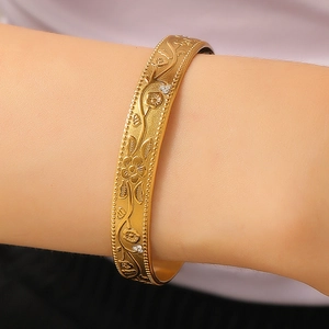 Detailed close-up of gold wide bangle featuring floral embossing and small white crystals