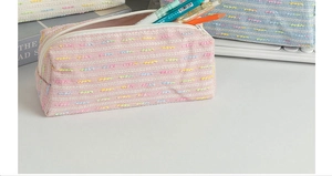 Detail of pink tweed pencil case with woven texture, top zipper, and colorful pattern
