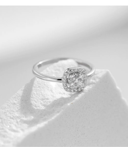 Macro shot of silver princess cut moissanite ring resting on a textured white stone