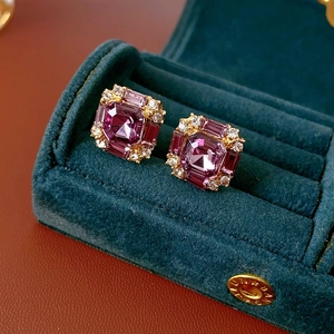 Macro shot of square purple gemstone stud earrings with diamonds in a green velvet box