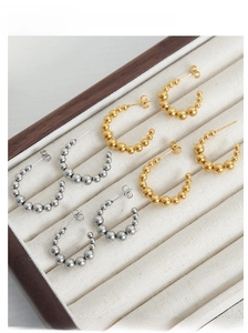 U-shaped beaded earrings in gold and silver finish on white velvet display tray