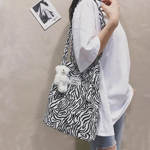 Zebra print canvas tote bag with a white plush bear charm and brand label detail