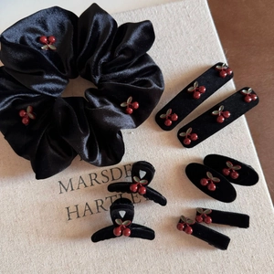 Flat lay of black velvet cherry hair accessories including clips and ties on a book